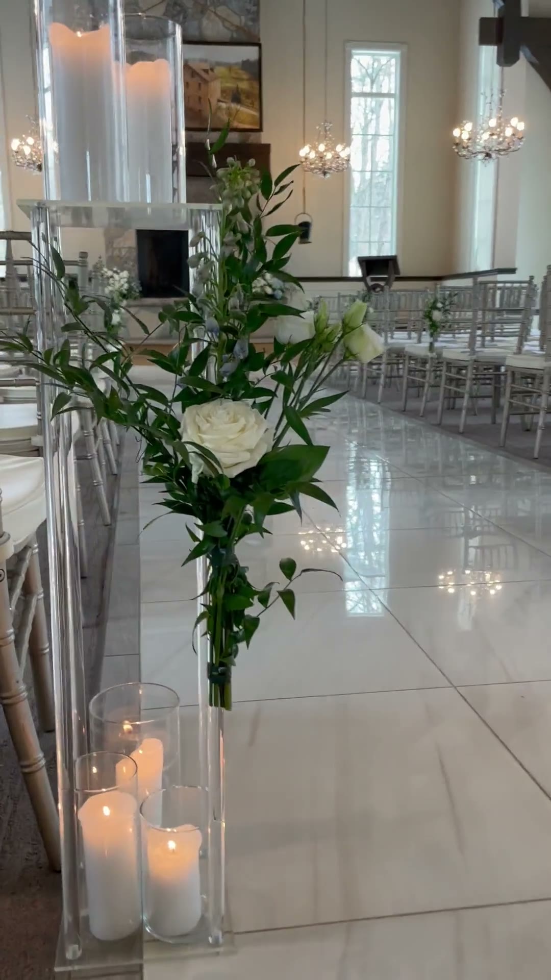 Ceremony aisle at Ancaster Mill Chapel lined with silver chairs, a white floral arrangement and candles