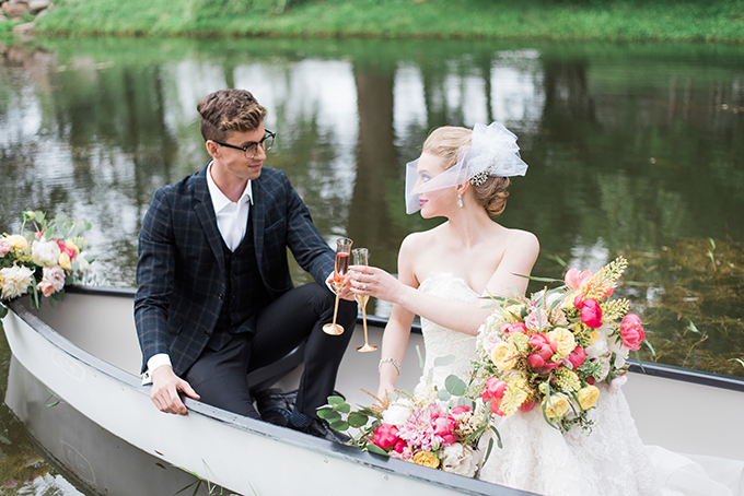 A couple toasting in a canoe on a pond at Mahraz Estate, with a bridal bouquet of pink, coral and yellow florals