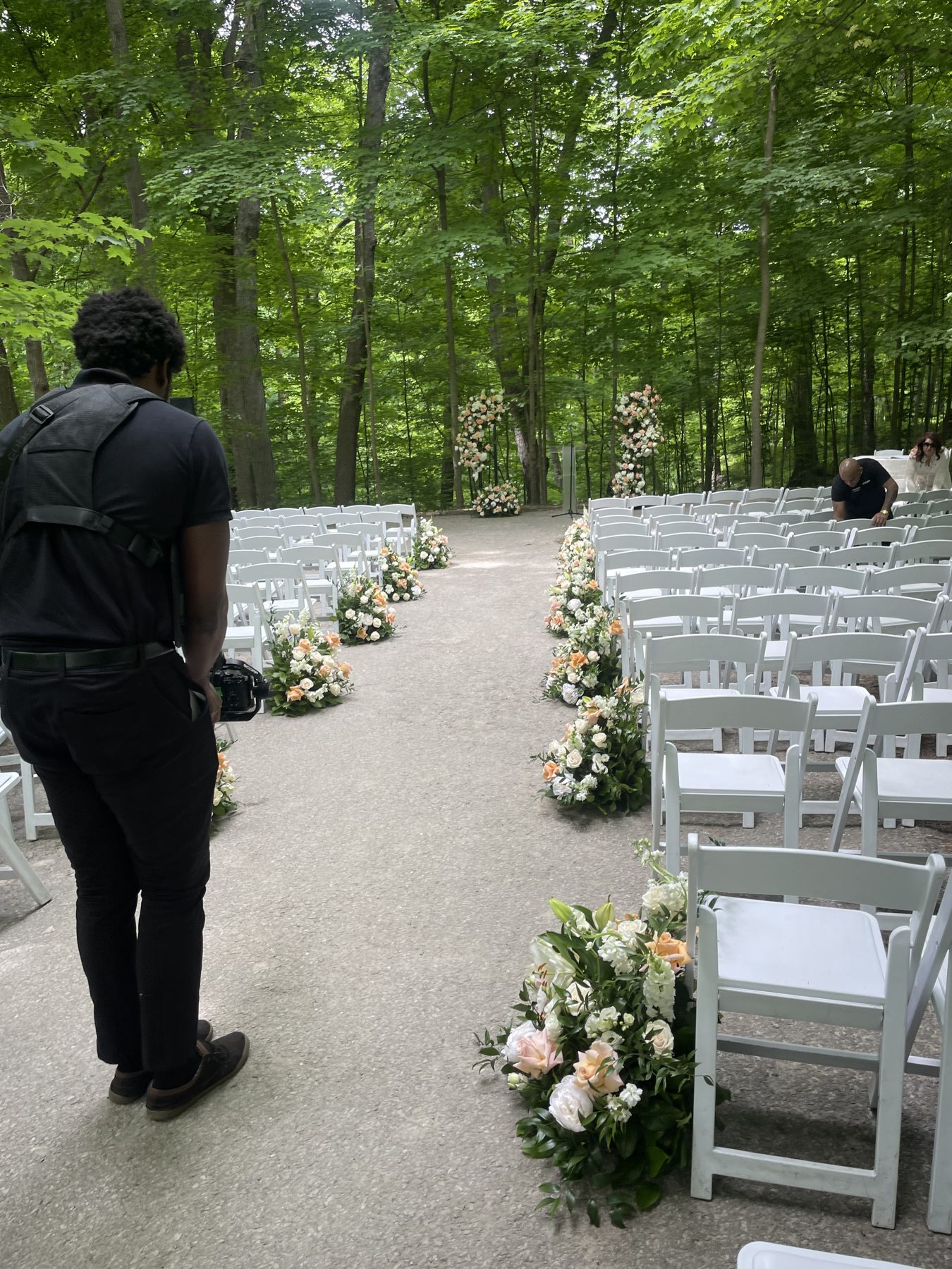 Woodland ceremony aisle at Hazelton Manor with white chairs, peach and cream floral arrangements along the rows and floral columns at the end